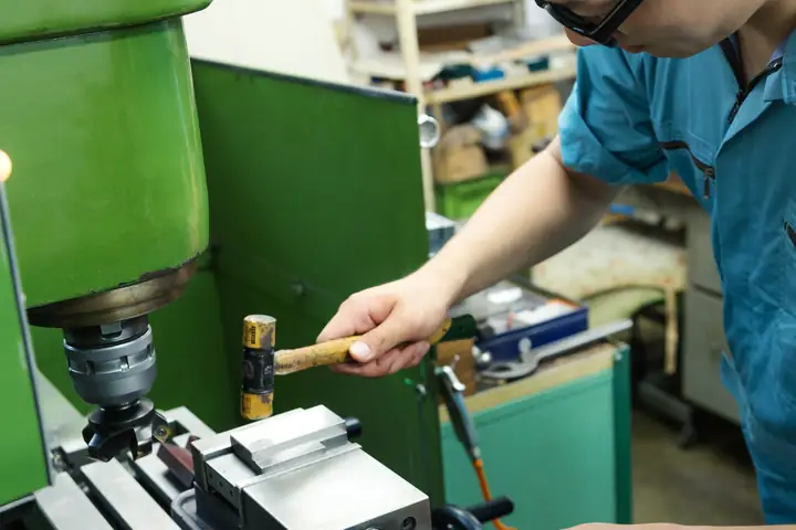 作業服の男性がフライス盤のハンドルを操作している